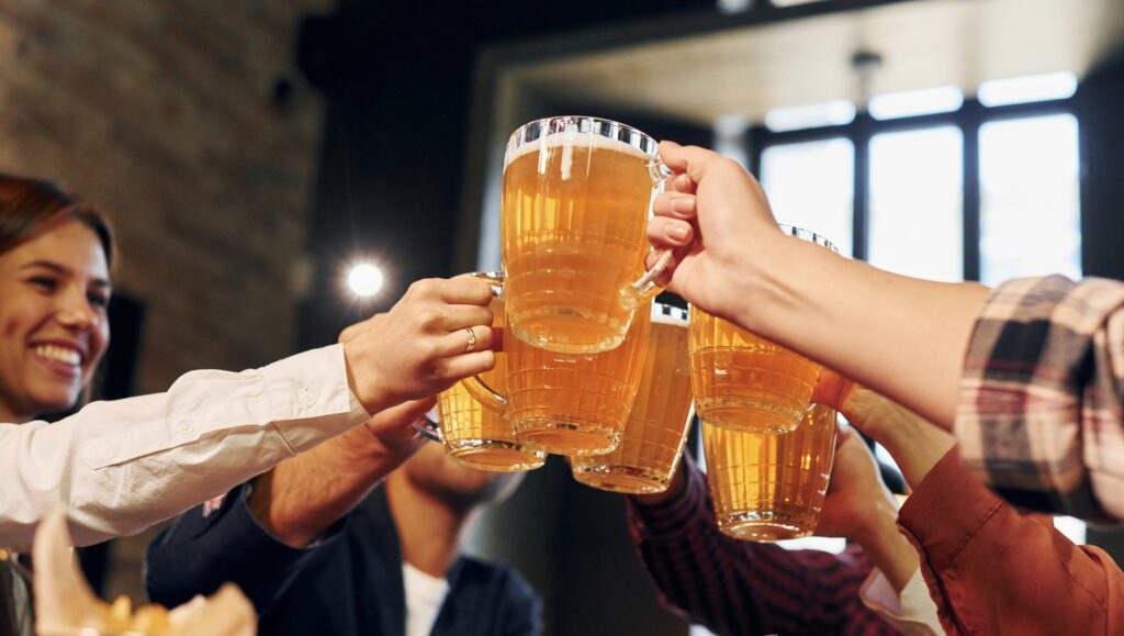 Cheering together. Group of young friends sitting in bar with beer